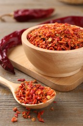 Aromatic spice. Red chili pepper flakes in bowl, spoon and pods on wooden table, closeup