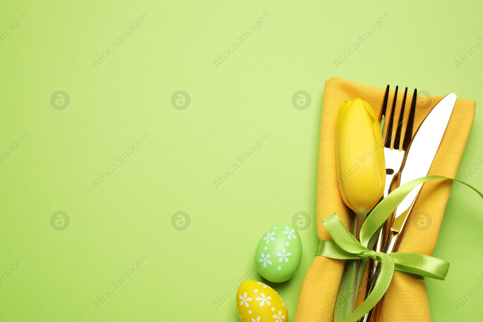 Photo of Top view of cutlery set with floral decor on green background, space for text. Easter celebration