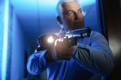 Photo of Professional security guard with gun checking dark room, focus on hand