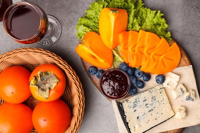 Delicious persimmon, blue cheese, blueberries and jam served on light grey table, flat lay