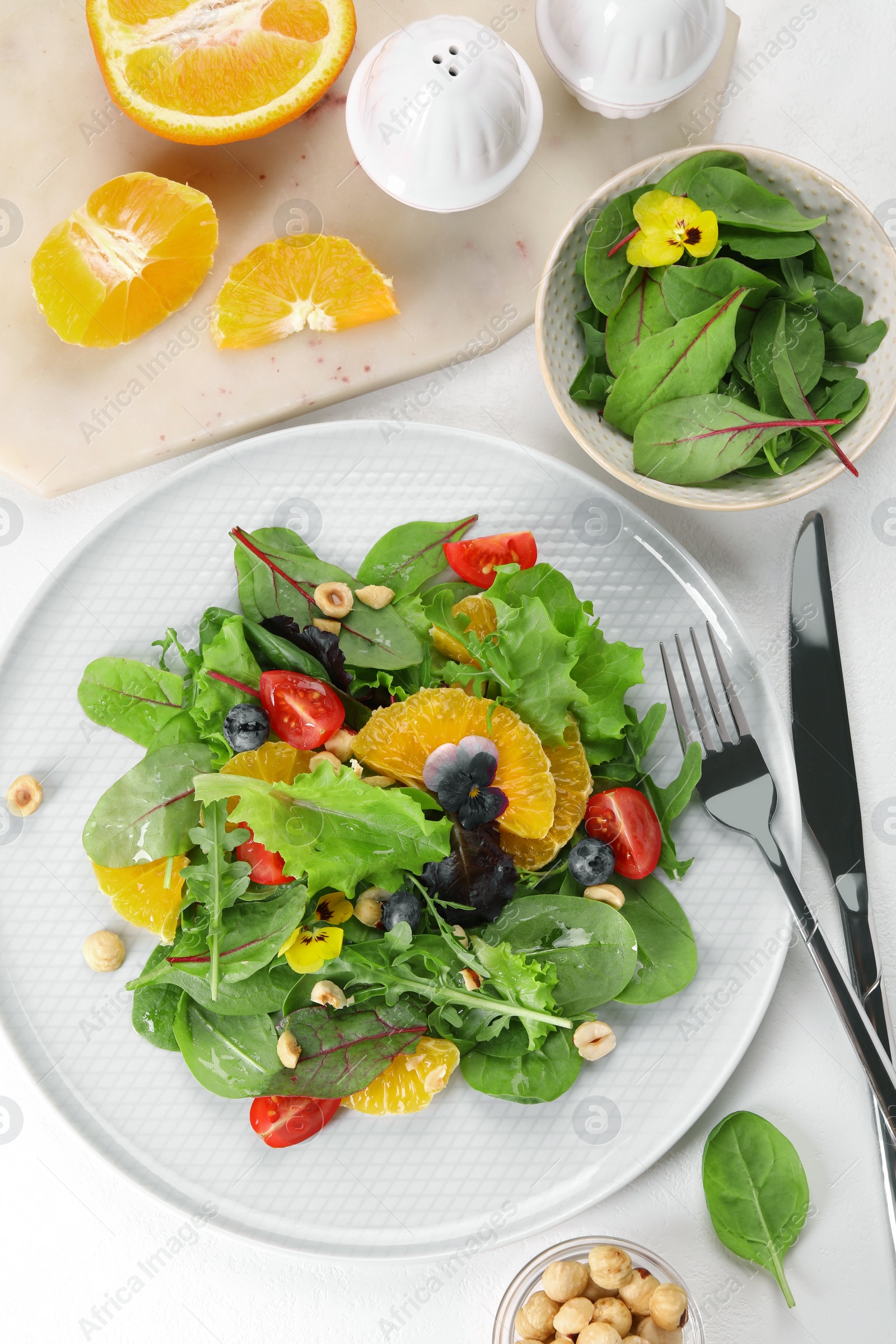 Photo of Delicious salad, ingredients and cutlery on white table, flat lay