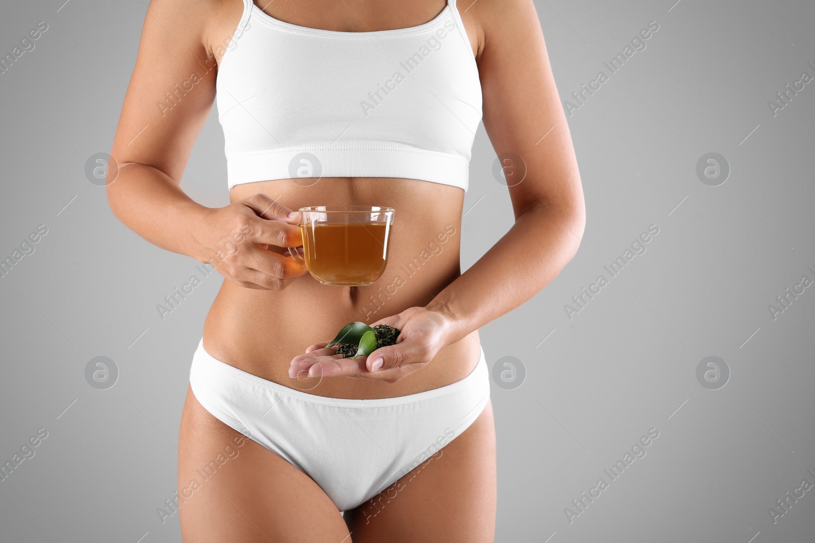 Photo of Young woman holding cup of diet tea, fresh and dry leaves on grey background, closeup