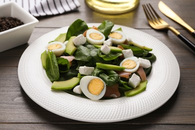 Photo of Delicious salad with boiled eggs, feta cheese and salmon on wooden table, closeup