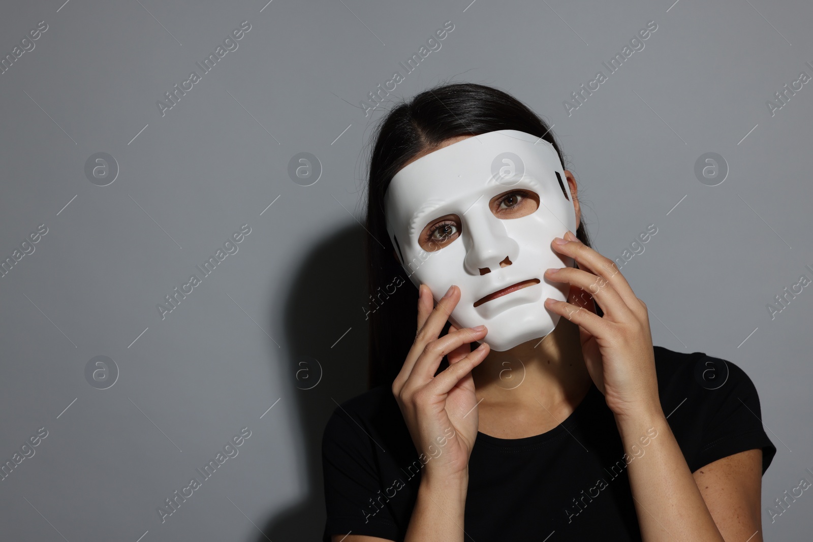 Photo of Multiple personality concept. Woman in mask on grey background, space for text