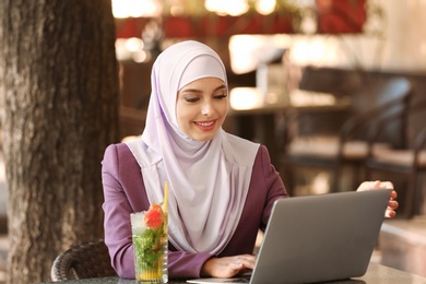 Photo of Muslim woman using laptop in outdoor cafe