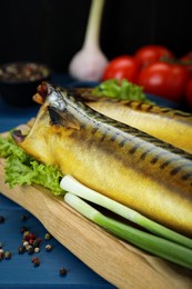 Delicious smoked mackerels, green onions and lettuce on blue table, closeup