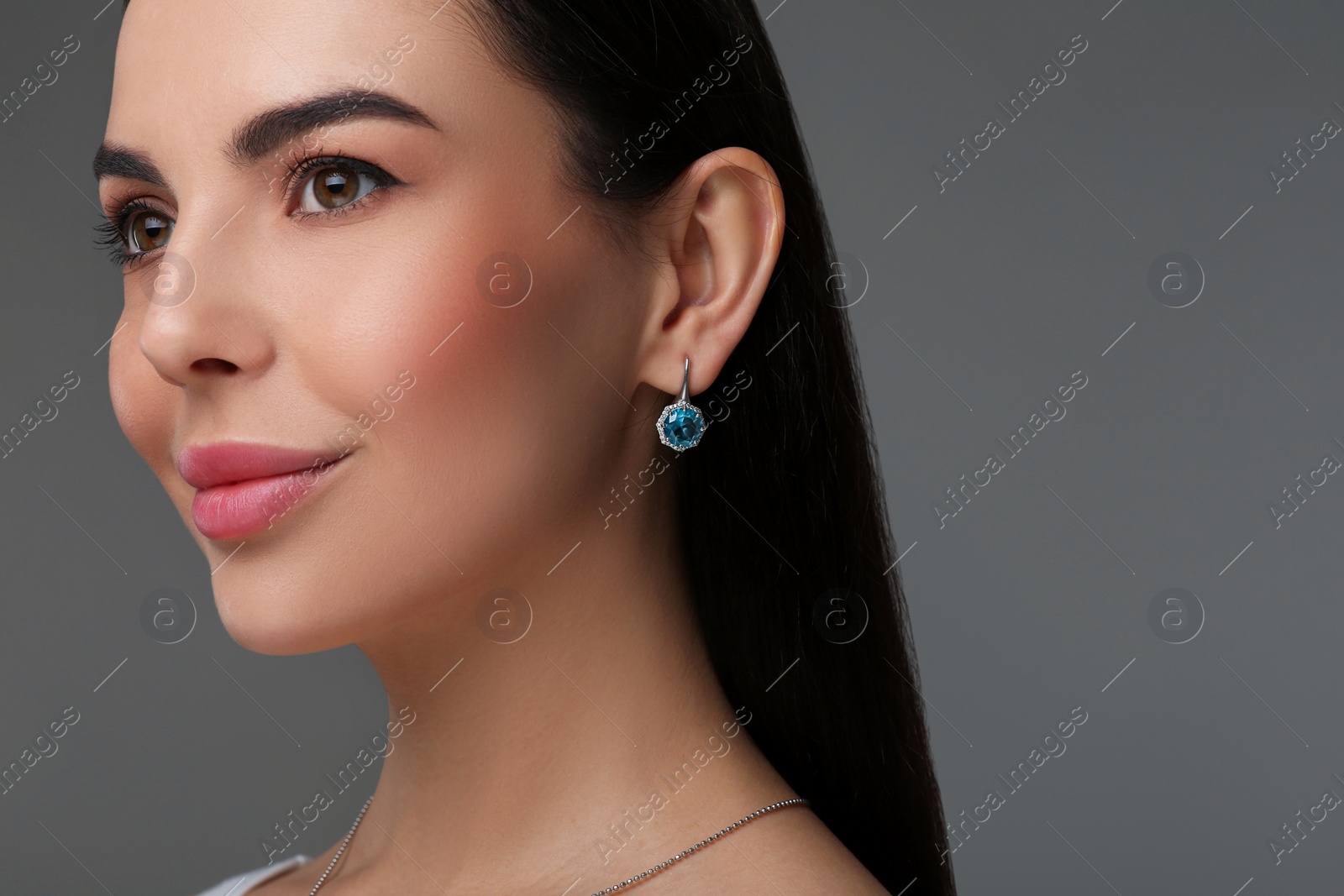 Photo of Beautiful young woman with elegant earrings on dark grey background, closeup