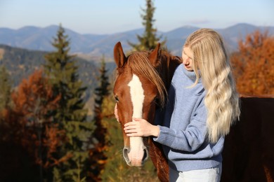 Young woman petting beautiful horse in mountains on sunny day