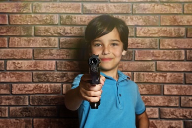 Little child playing with gun against brick wall. Dangerous game