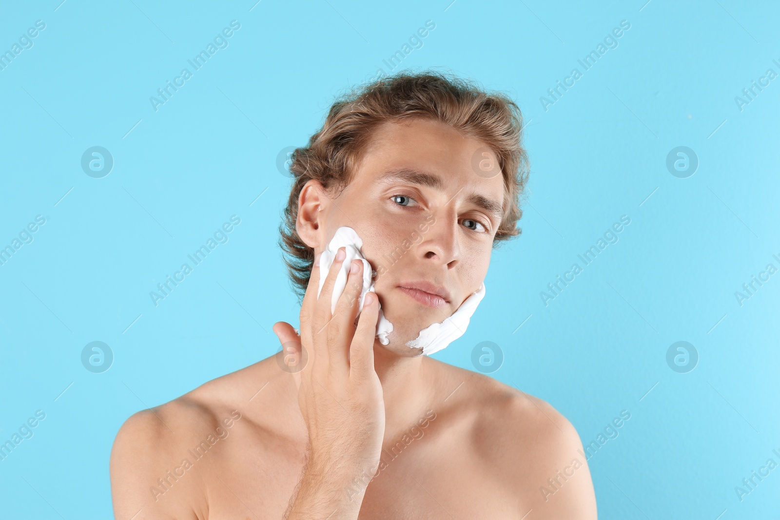 Photo of Young man applying shaving foam on color background