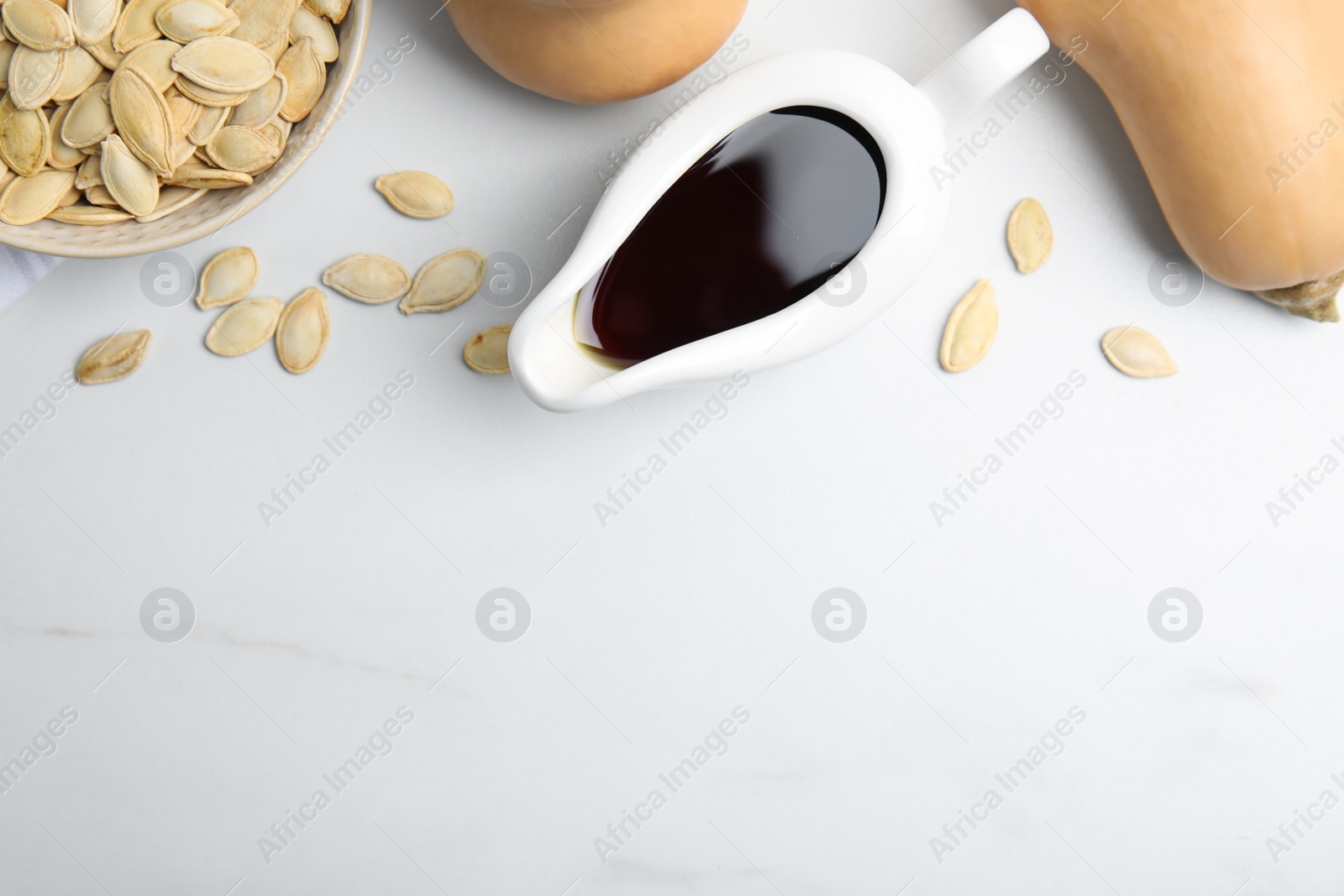 Photo of Gravy boat of oil, pumpkins and seeds on white table, flat lay. space for text