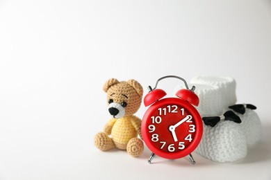Photo of Alarm clock, toy bear and baby booties on white background, space for text. Time to give birth