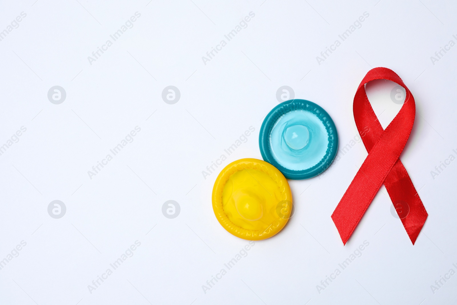 Photo of Colorful condoms and red ribbon on white background, top view. LGBT concept