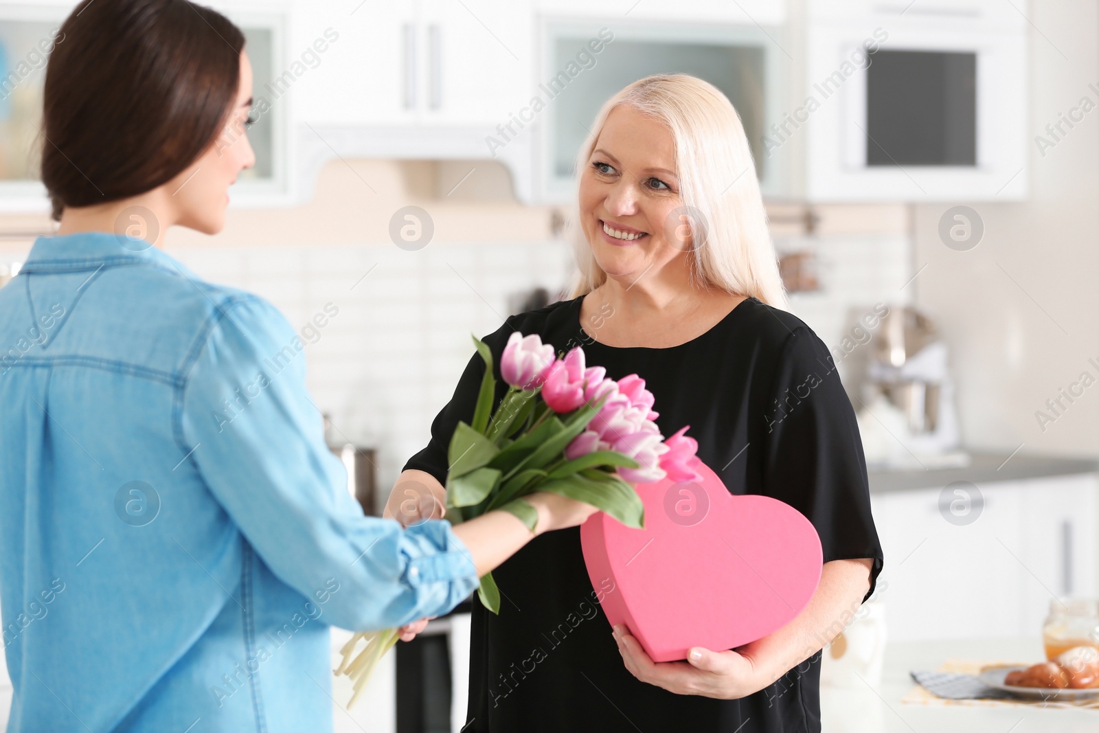 Photo of Daughter congratulating happy mature woman on Mother's Day at home