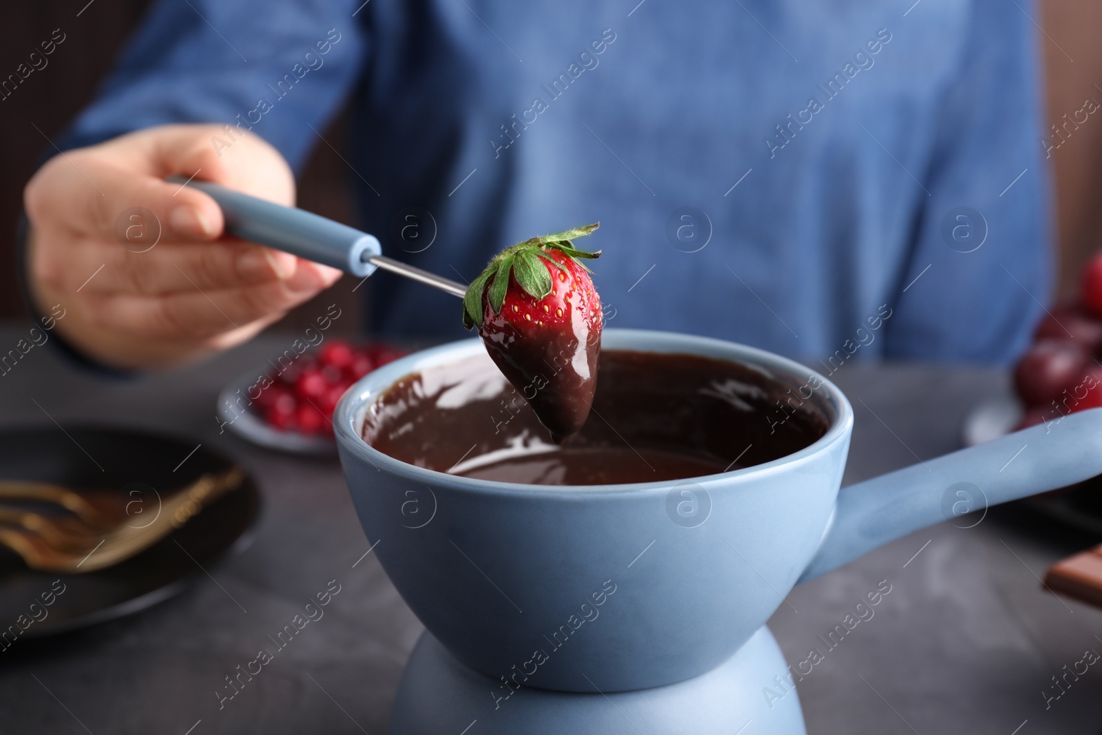 Photo of Woman dipping strawberry into pot with chocolate fondue at table, closeup