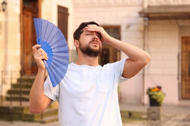 Man with hand fan suffering from heat outdoors