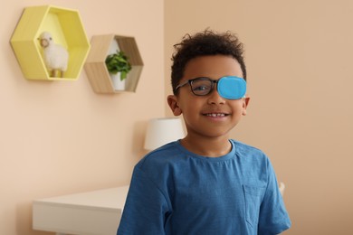 African American boy with eye patch on glasses in room, space for text. Strabismus treatment