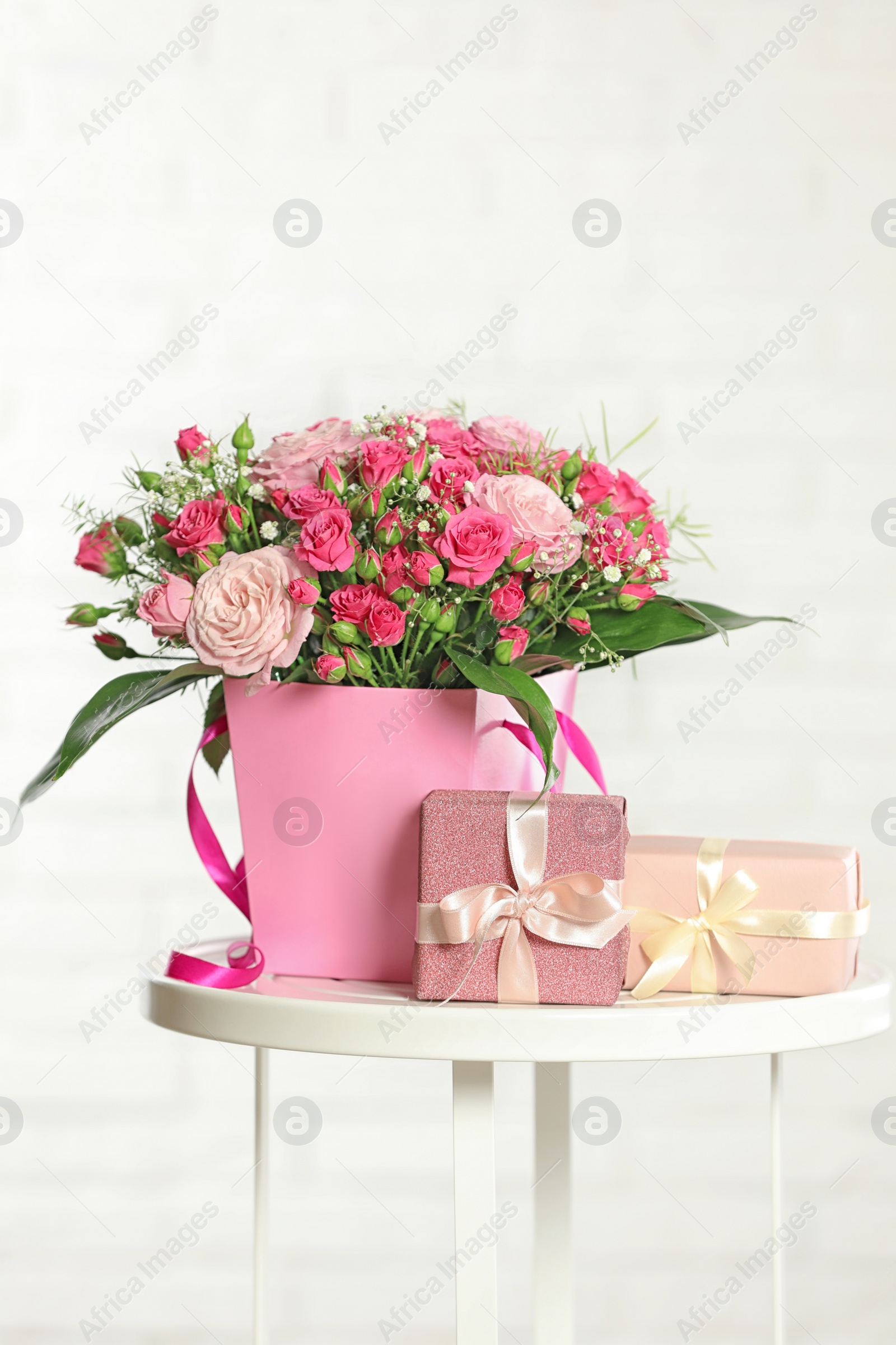 Photo of Beautiful bouquet of flowers and gift boxes on table against light background