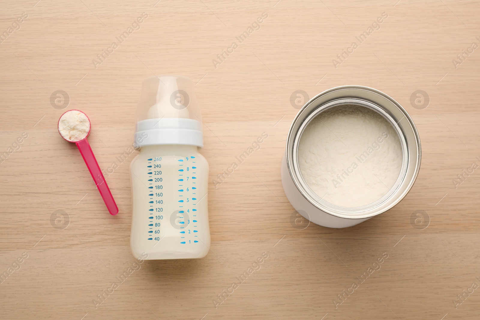 Photo of Feeding bottle with infant formula and powder on wooden table, flat lay