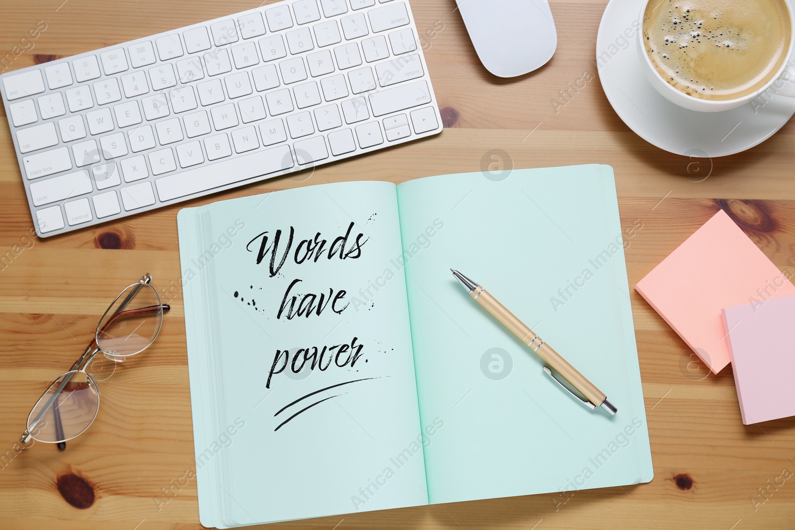 Image of Open notebook with phrase Words Have Power and pen on wooden table, flat lay. Workplace with cup of coffee