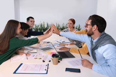 Photo of Team of employees joining hands at white table in office. Startup project
