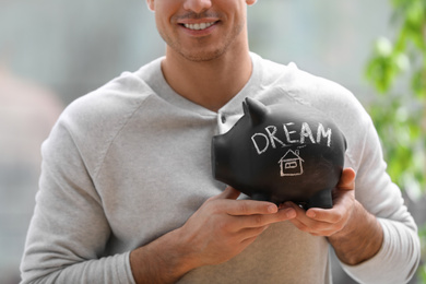 Man holding piggy bank with word DREAM against blurred background, closeup