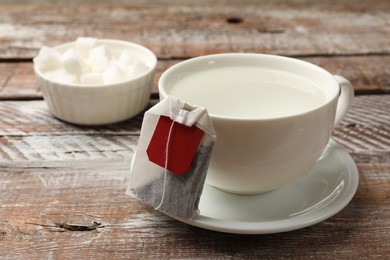 Photo of Tea bag and cup with hot water on wooden rustic table, closeup