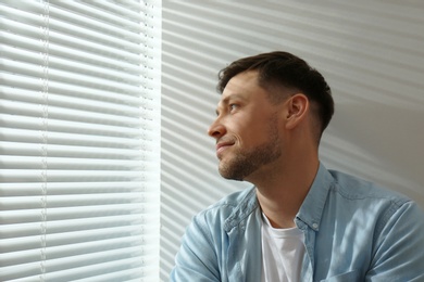 Photo of Handsome man near window with Venetian blinds. Space for text