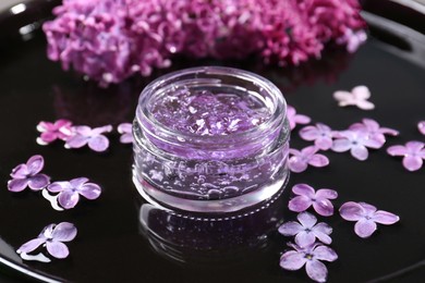 Photo of Jar of cosmetic product and lilac flowers on black surface