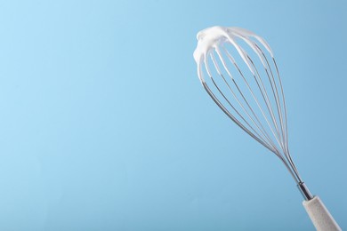Whisk with whipped cream on light blue background. Space for text