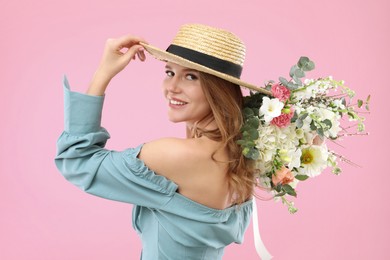 Photo of Beautiful woman in straw hat with bouquet of flowers on pink background