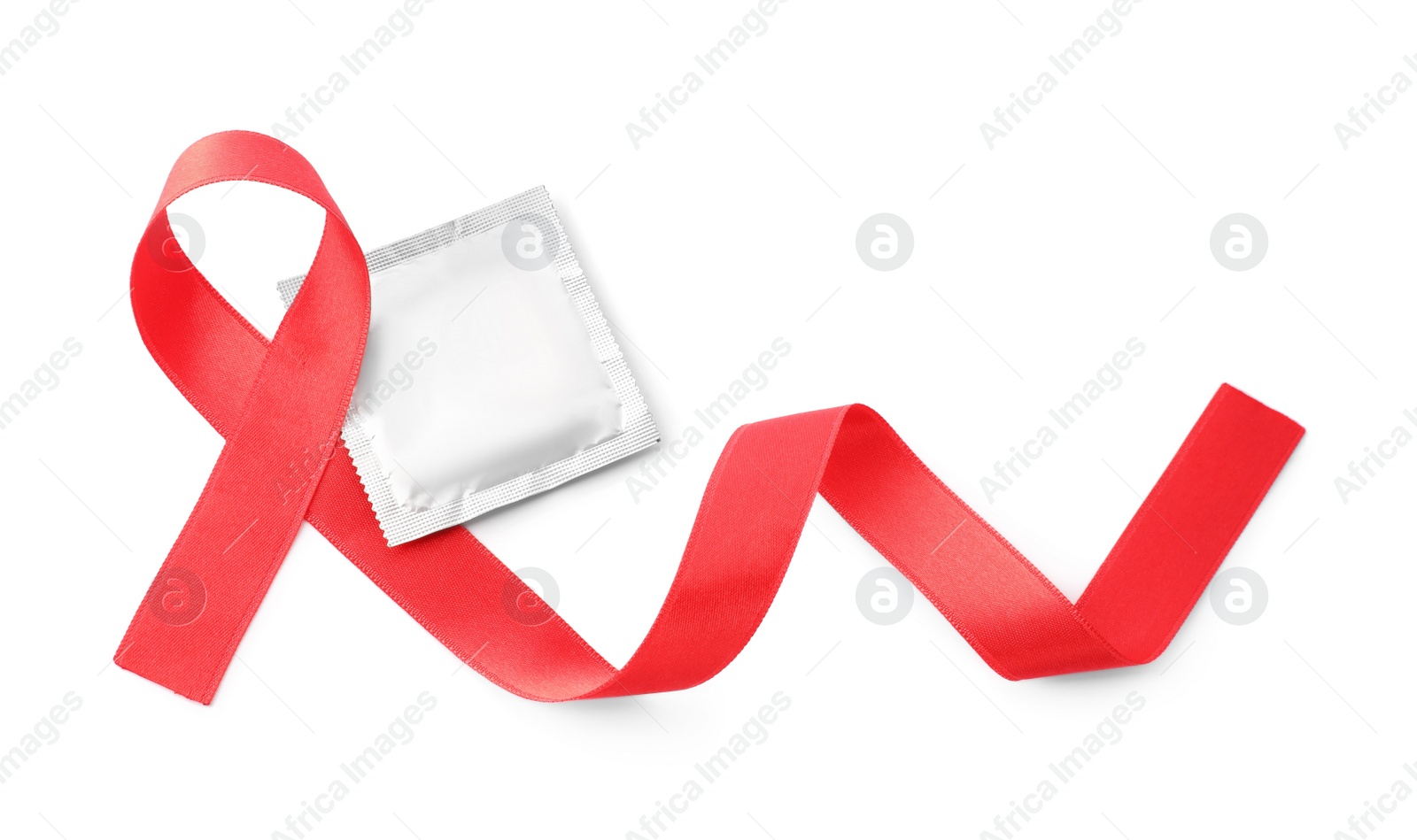 Photo of Red ribbon and condom isolated on white, top view. AIDS disease awareness