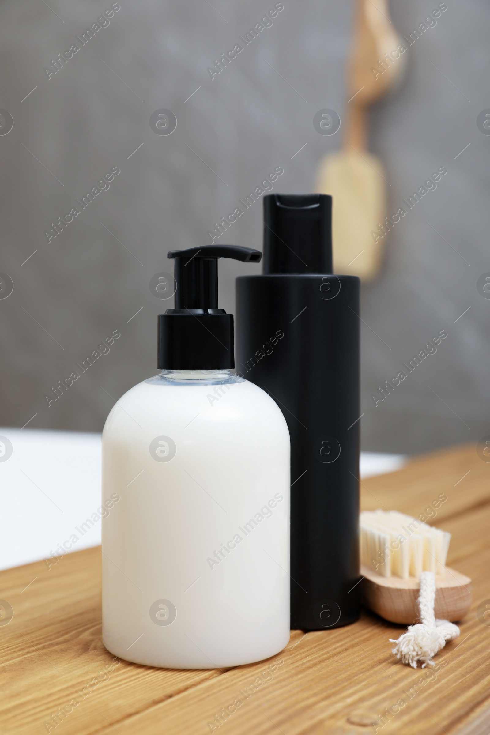 Photo of Bottles of shower gels and brush on wooden table in bathroom