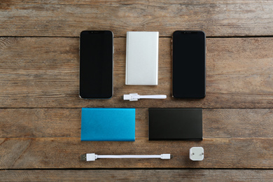 Photo of Flat lay composition with mobile phones and portable chargers on wooden background