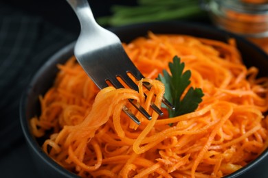 Photo of Fork with Korean carrot salad over bowl, closeup
