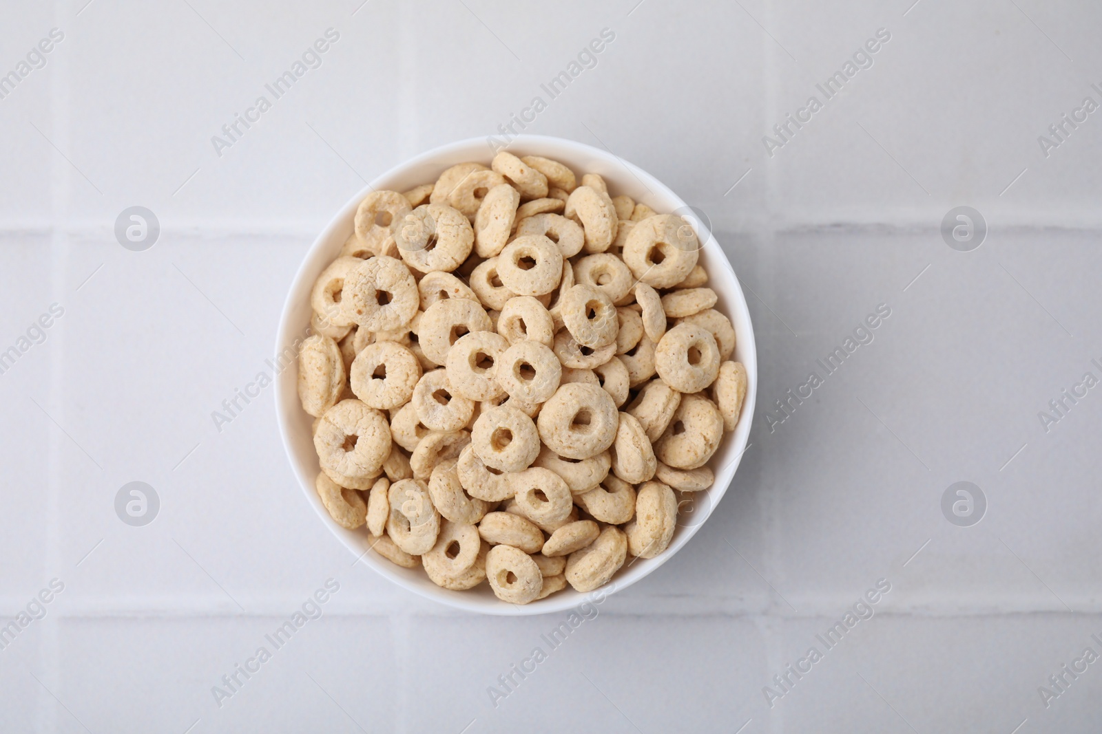 Photo of Tasty cereal rings in bowl on white tiled table, top view