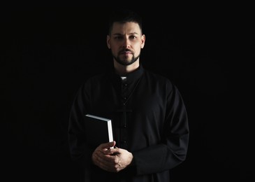 Priest in cassock with Bible on dark background