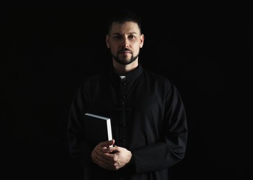 Photo of Priest in cassock with Bible on dark background