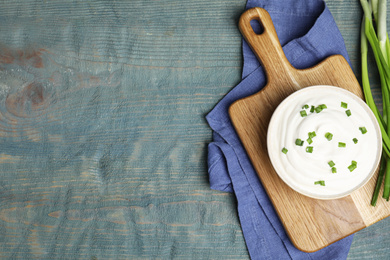 Photo of Fresh sour cream with onion on light blue wooden table, flat lay. Space for text