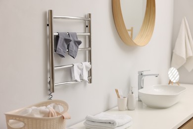 Photo of Heated towel rail with socks on white wall in bathroom