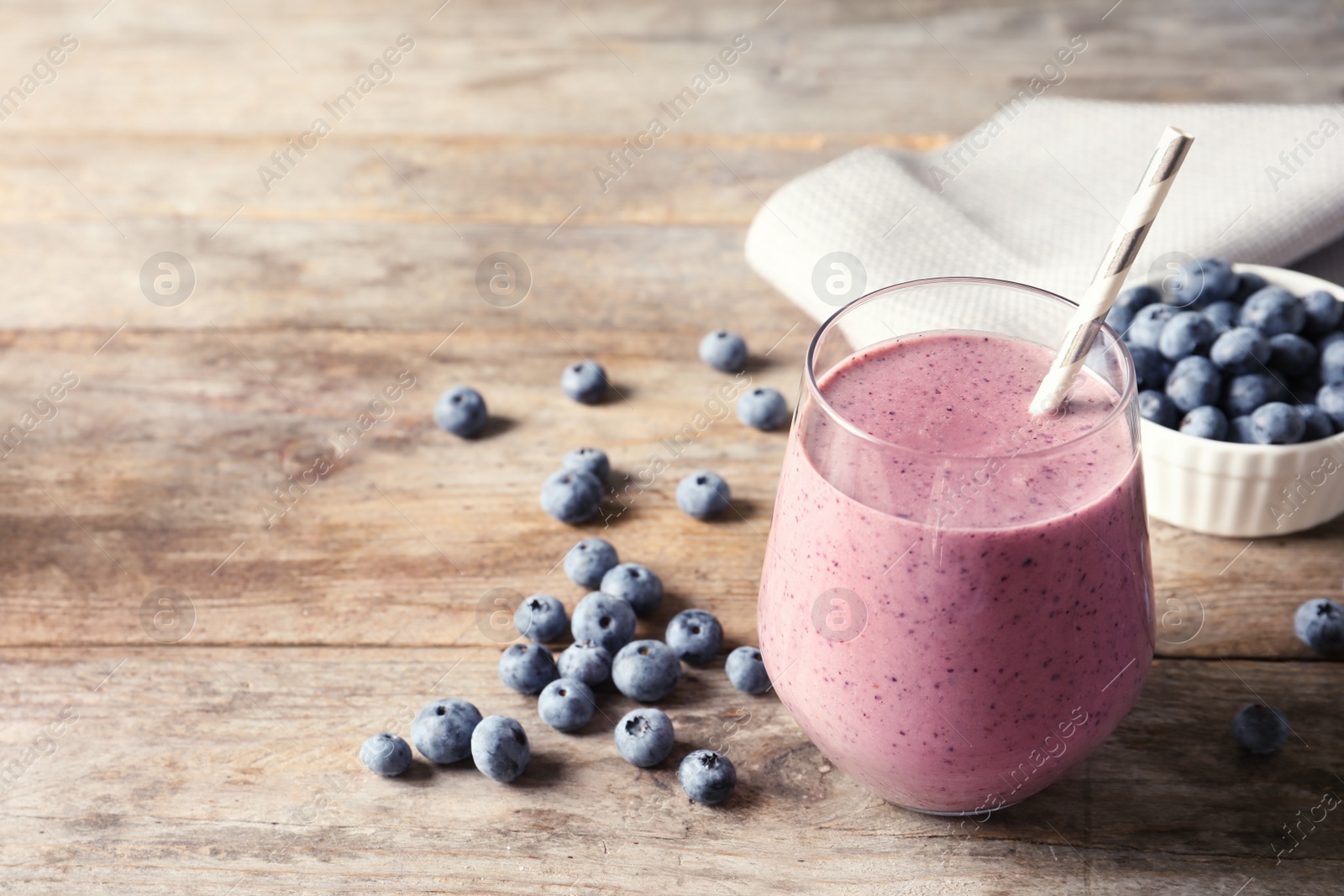 Photo of Tasty blueberry smoothie in glass, berries and space for text on wooden table