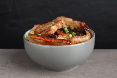 Photo of Bowl with tasty fried pork fatback slices and green onion on grey table