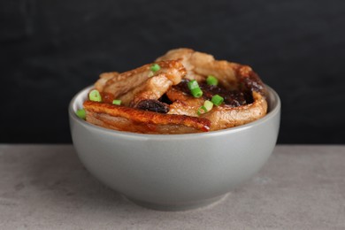 Bowl with tasty fried pork fatback slices and green onion on grey table