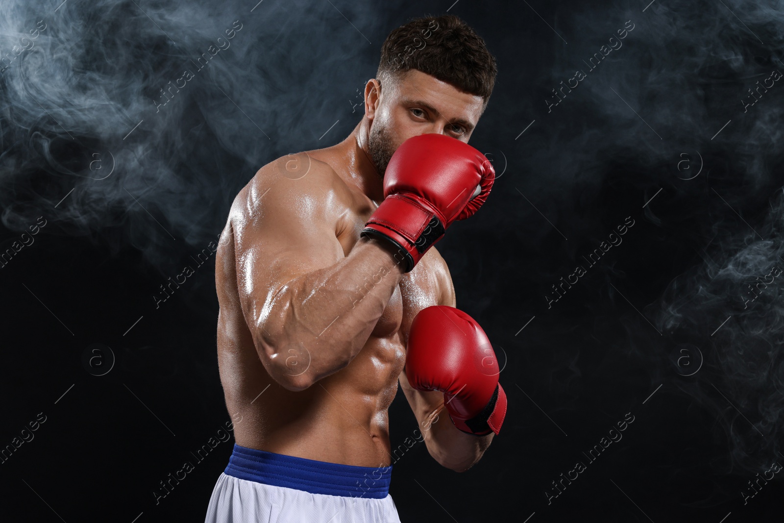 Photo of Man wearing boxing gloves in smoke on black background. Space for text