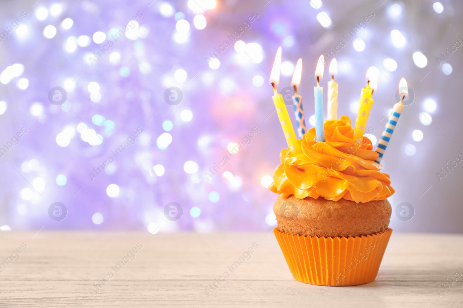 Photo of Delicious birthday cupcake with candles on table against blurred background