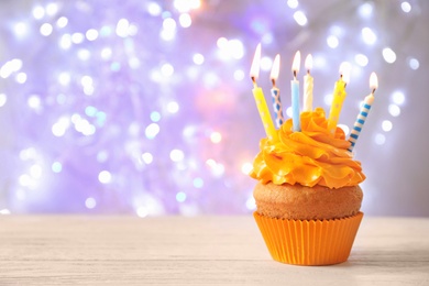 Photo of Delicious birthday cupcake with candles on table against blurred background