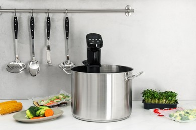 Sous vide cooker in pot and ingredients on white table. Thermal immersion circulator