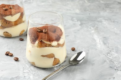 Photo of Delicious tiramisu in glasses, coffee beans and spoon on grey textured table, space for text