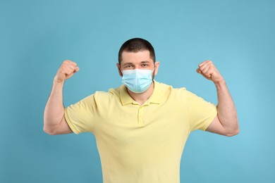 Photo of Man with protective mask showing muscles on light blue background. Strong immunity concept