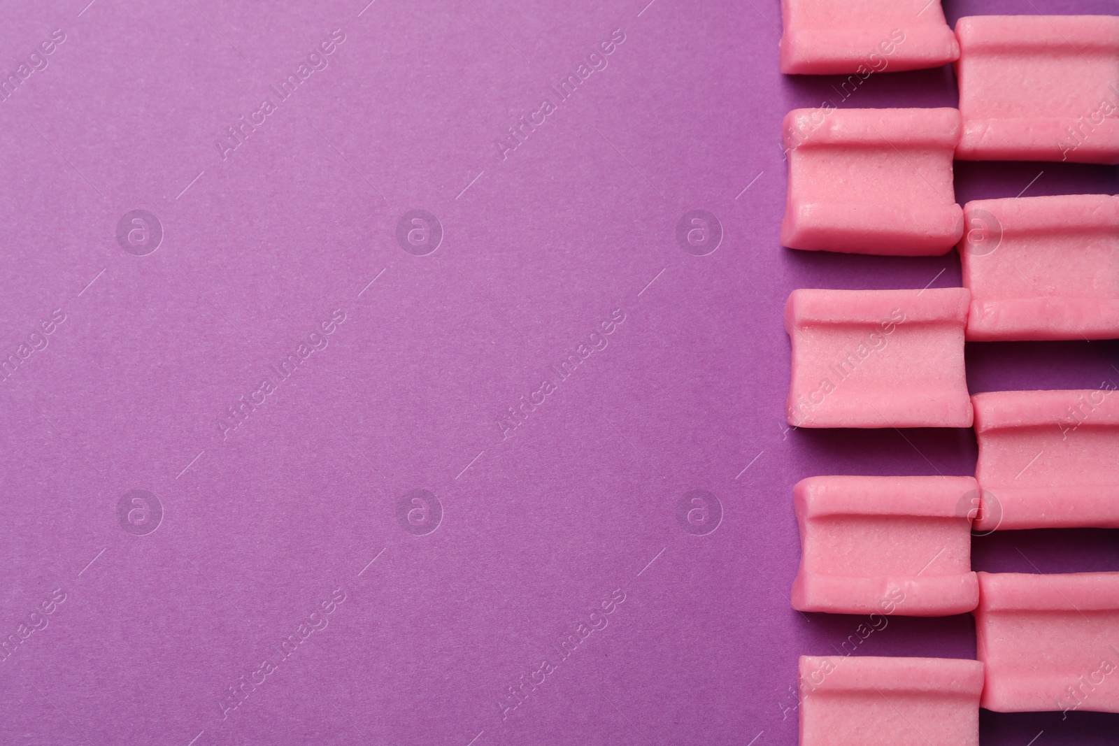 Photo of Tasty pink chewing gums on purple background, flat lay. Space for text